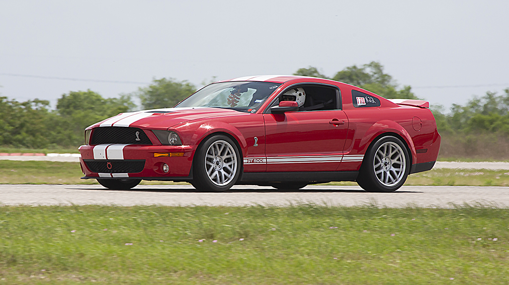Action shot of a Red 2008 Ford Shelby GT500 Mustang driving on the road course at Mustang Week Texas 2026