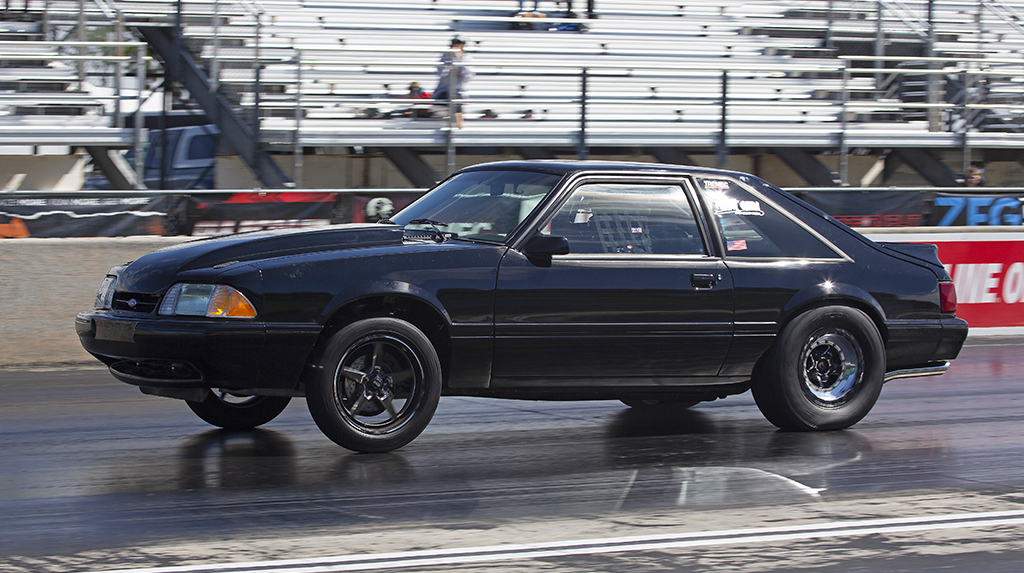 A black 1993 Ford Mustang hatchback with the front wheels partially lifted races down the dragstrip at South Georgia Motorsports Park during the 2026 Mod Motor Nationals